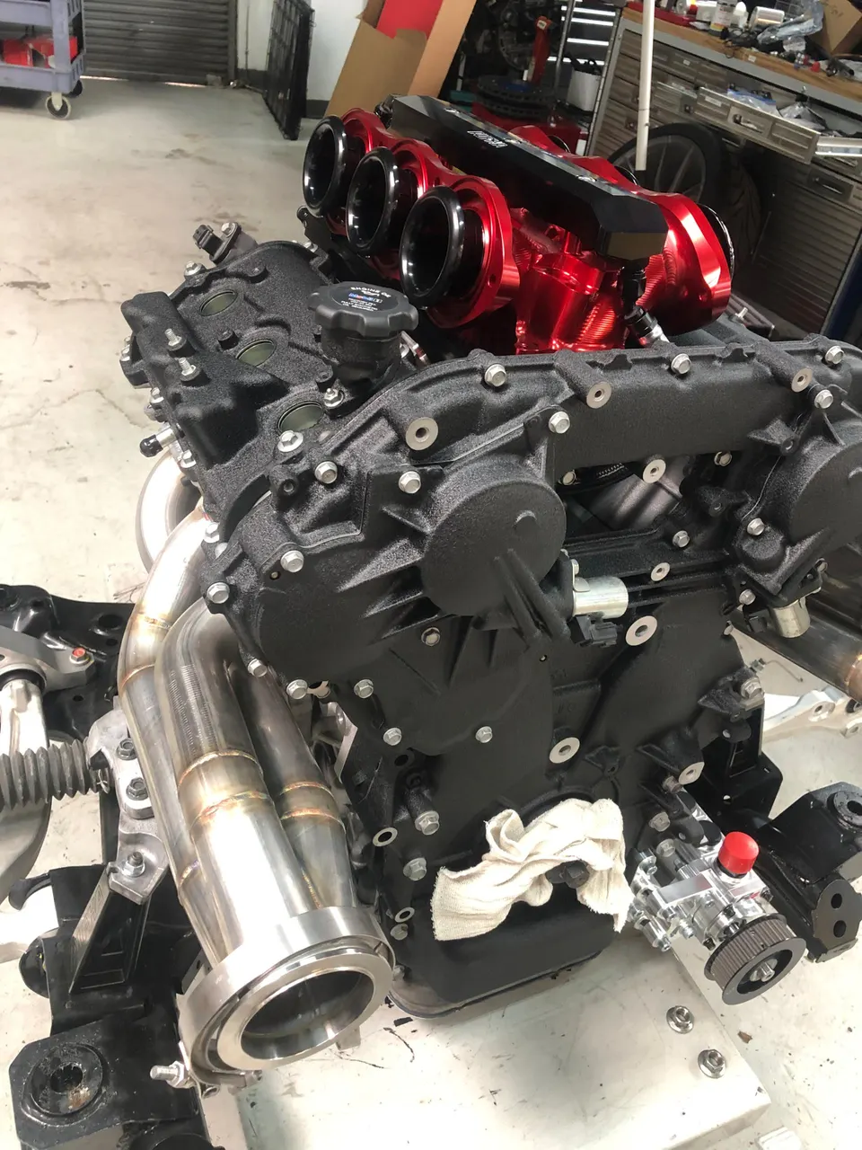 High-performance engine assembly with red individual throttle body intake manifold and custom exhaust headers in a shop.