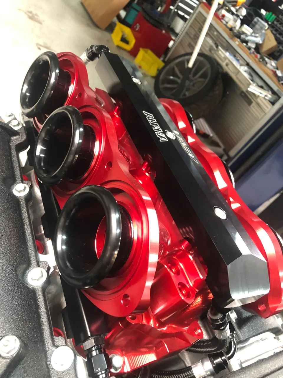 Red Alpha Performance intake manifold with velocity stacks installed in an engine bay at a performance shop.