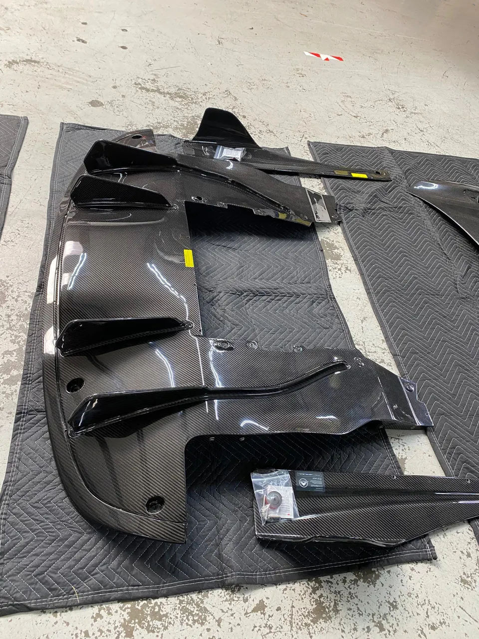 New carbon fiber aerodynamic parts, including a diffuser and underbody panels, laid out on blankets in a shop.