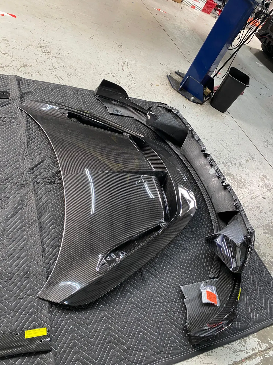 Carbon fiber exterior aerodynamic parts laid out on a protective mat in a performance tuning shop.