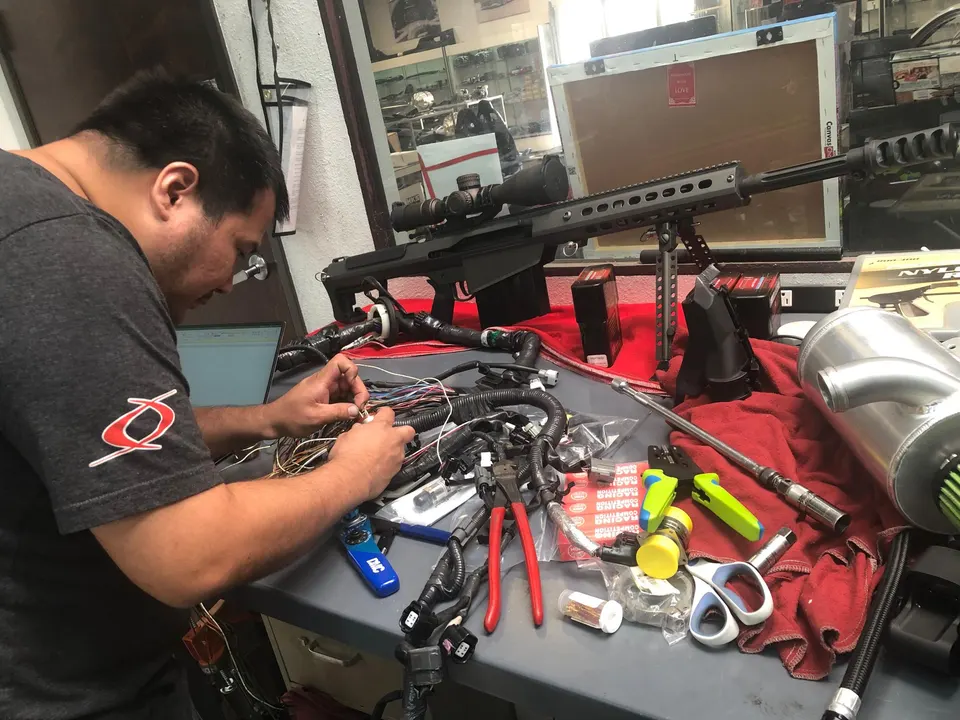 A Jotech technician meticulously working on a complex wiring harness with various tools and a laptop in a performance tuning shop.