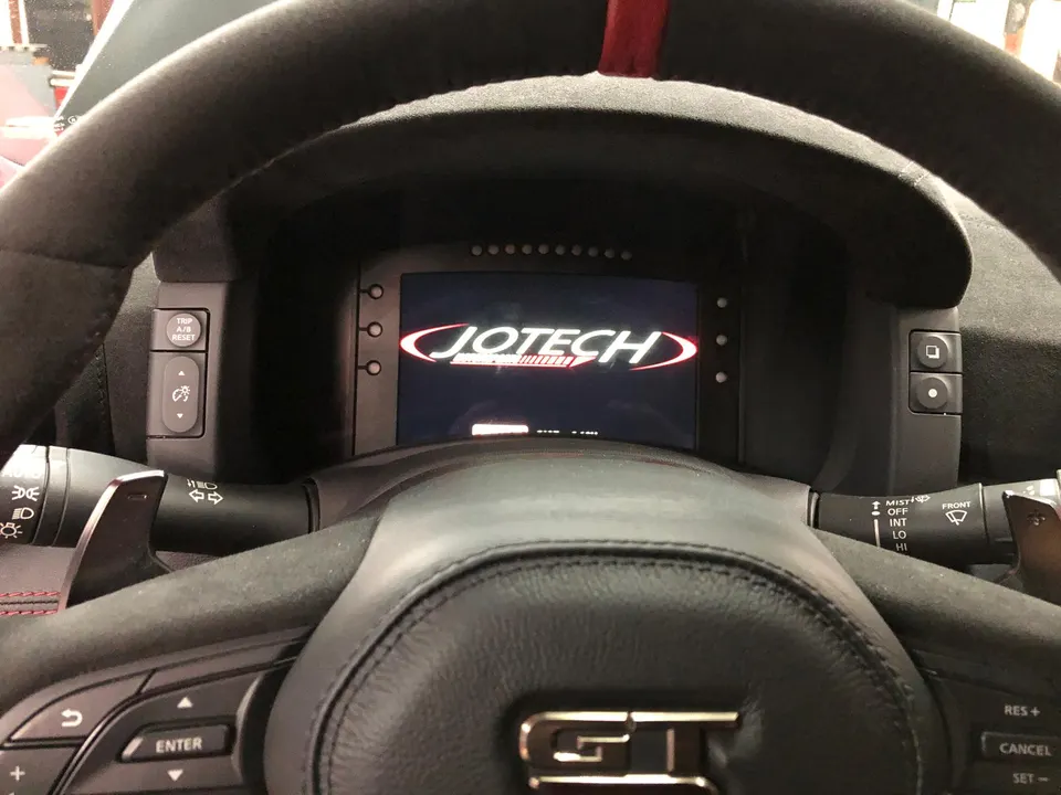 Close-up of a Nissan GT-R interior showing the steering wheel and a Jotech digital dashboard.