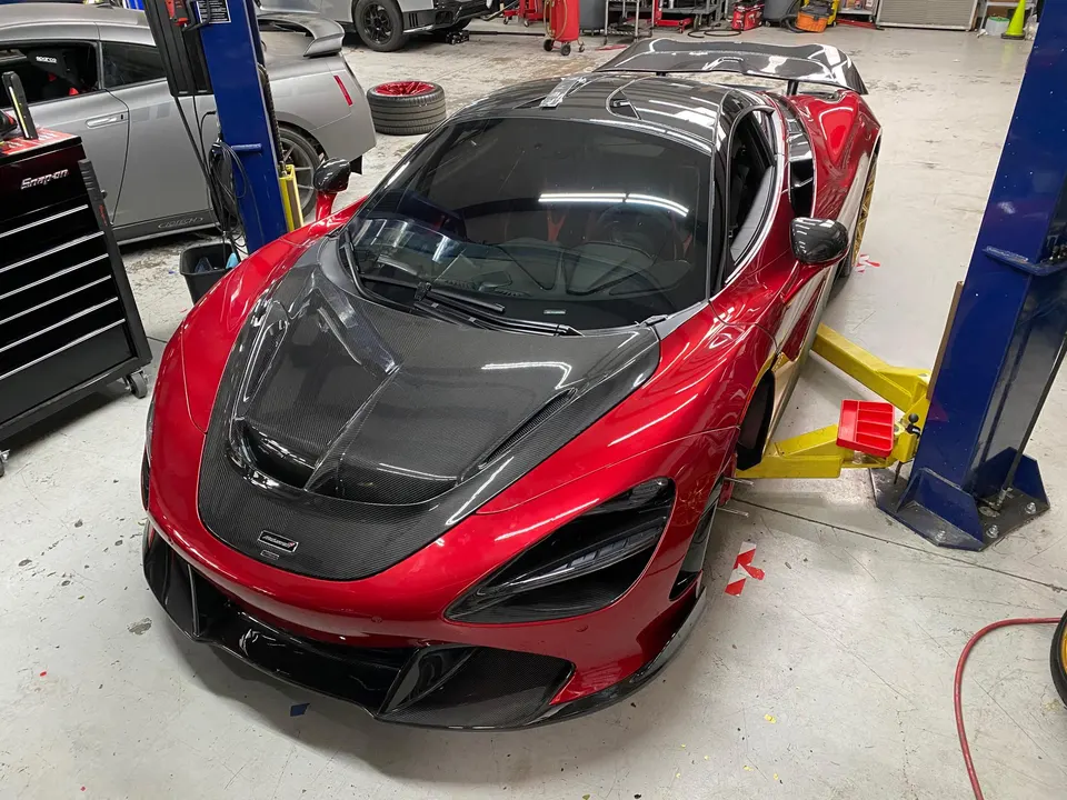A red McLaren 720S with carbon fiber hood and aero parts on a car lift inside a Jotech Motorsports performance shop.