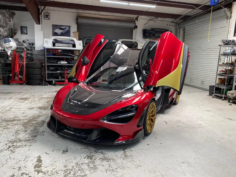 A red and gold McLaren 720S with its butterfly doors open, parked inside a performance tuning shop.