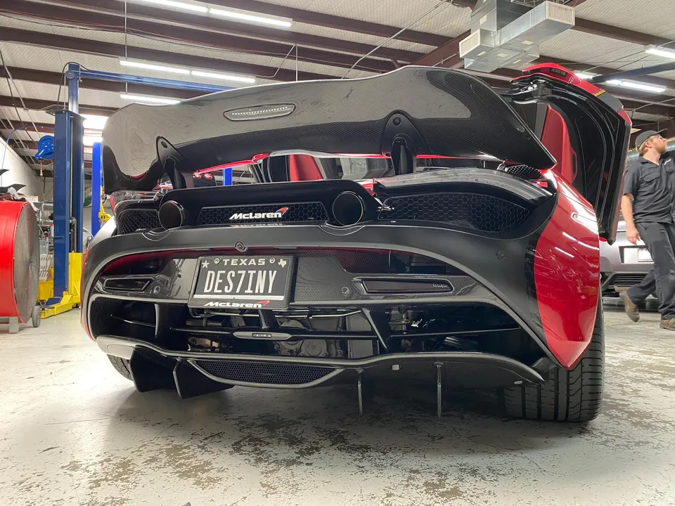 A red McLaren with a large carbon fiber wing and diffuser in a performance tuning shop.