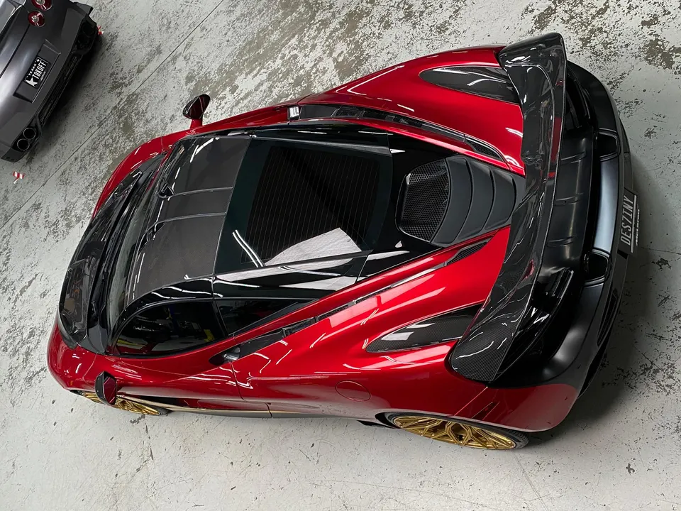 Overhead view of a red McLaren supercar with a carbon fiber rear wing and gold wheels parked in a garage.