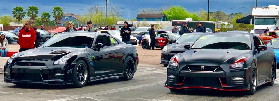 Two modified Nissan GT-R R35s lined up at a drag strip, ready for a race, with spectators in the background.