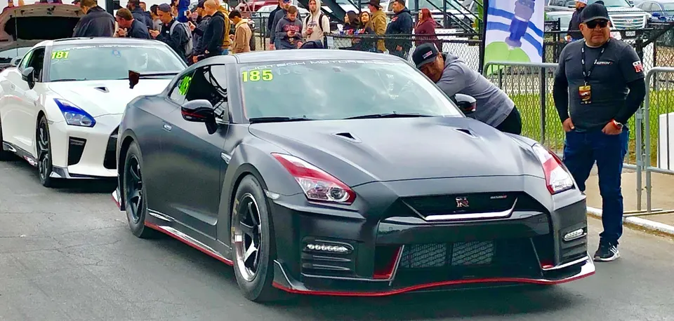 Two Nissan GT-R R35s, one matte black and one white, in the staging lanes at a drag strip event.