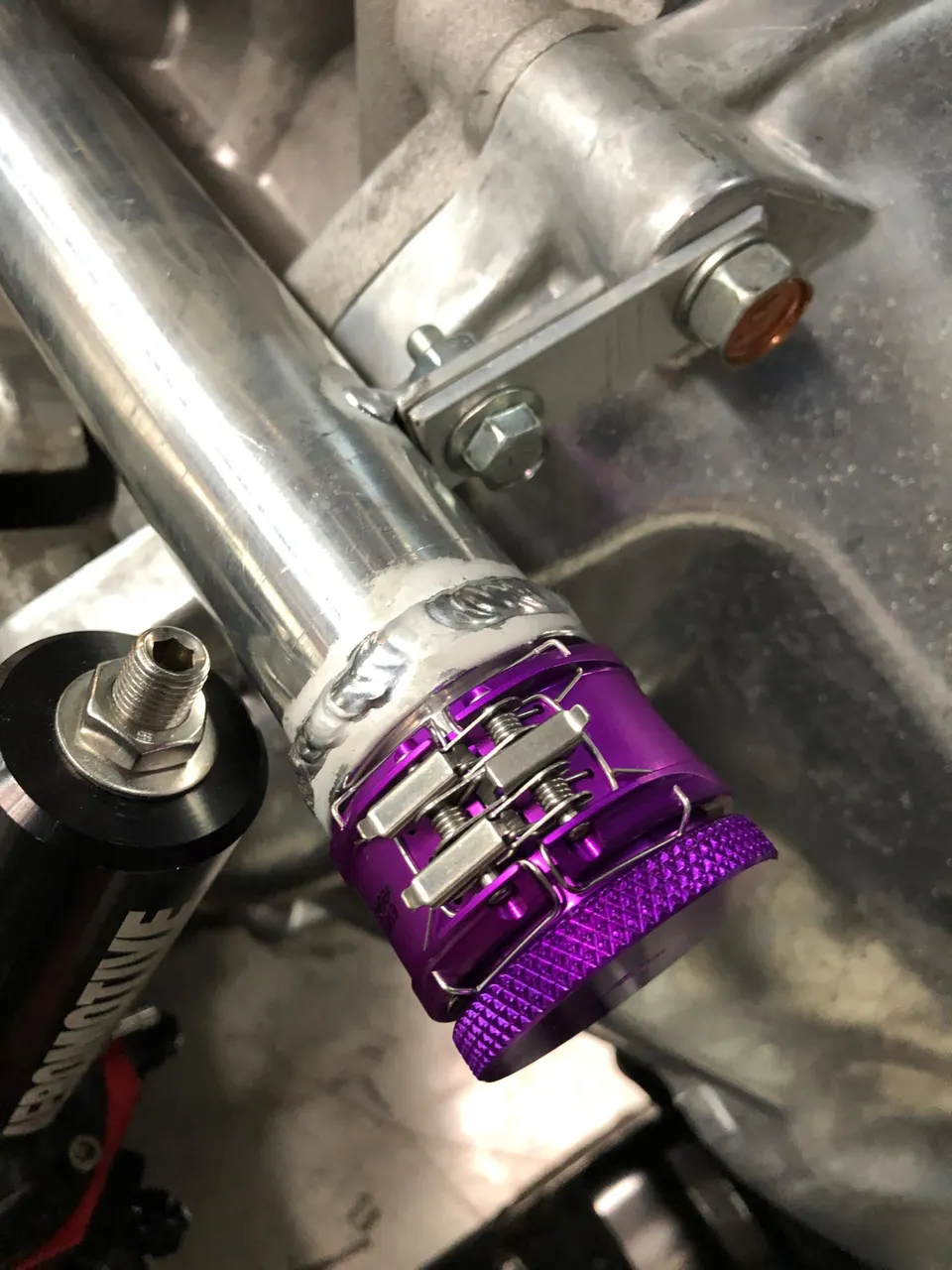 Close-up of a purple quick-release V-band clamp on an aluminum pipe in a high-performance engine bay.