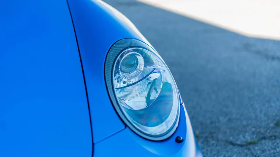 Close-up of a blue Porsche headlight, showcasing the intricate design and clear lens.