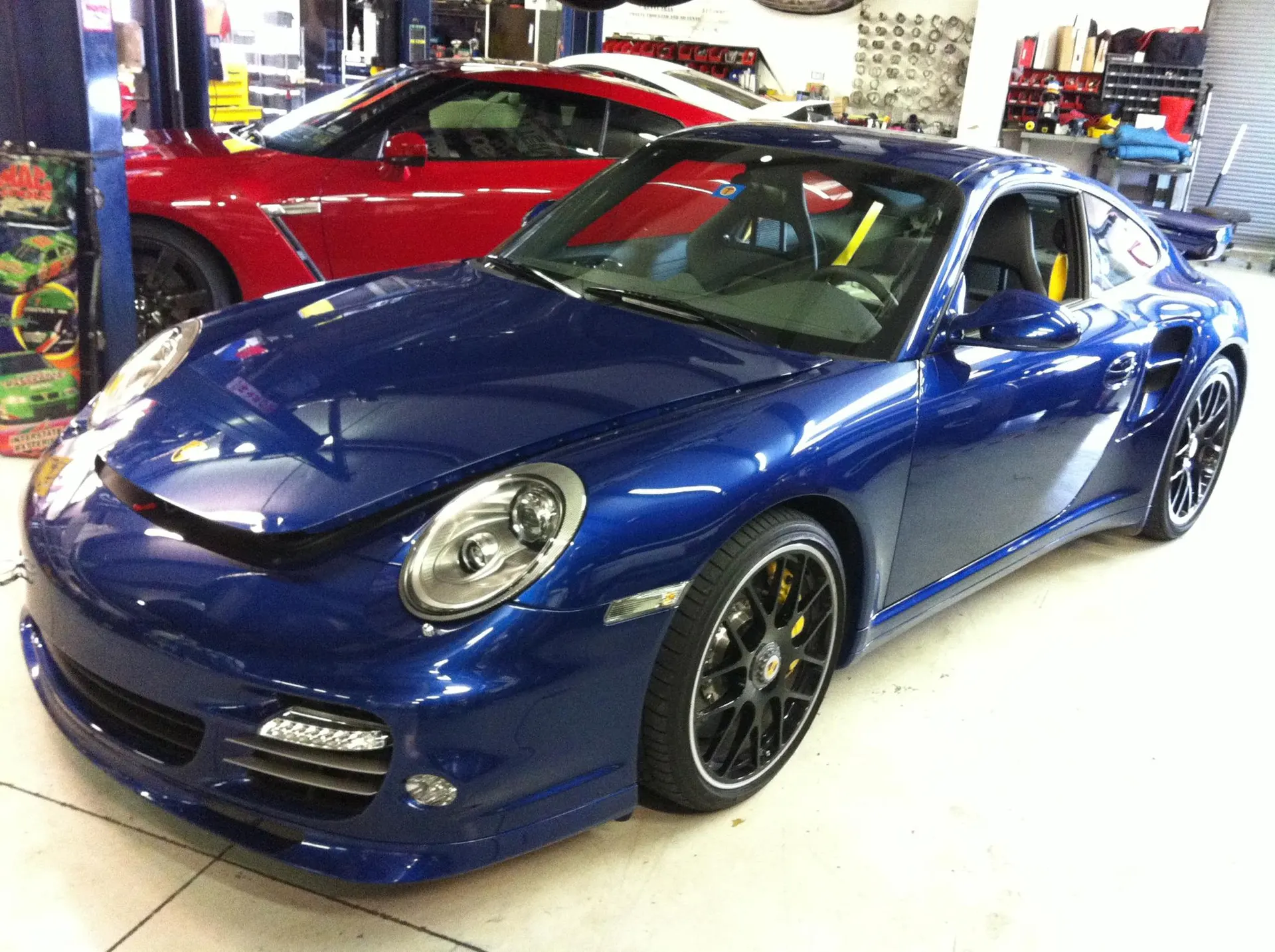 Blue Porsche 911 Turbo and red Nissan GT-R parked inside a performance tuning shop with lifts in the background.