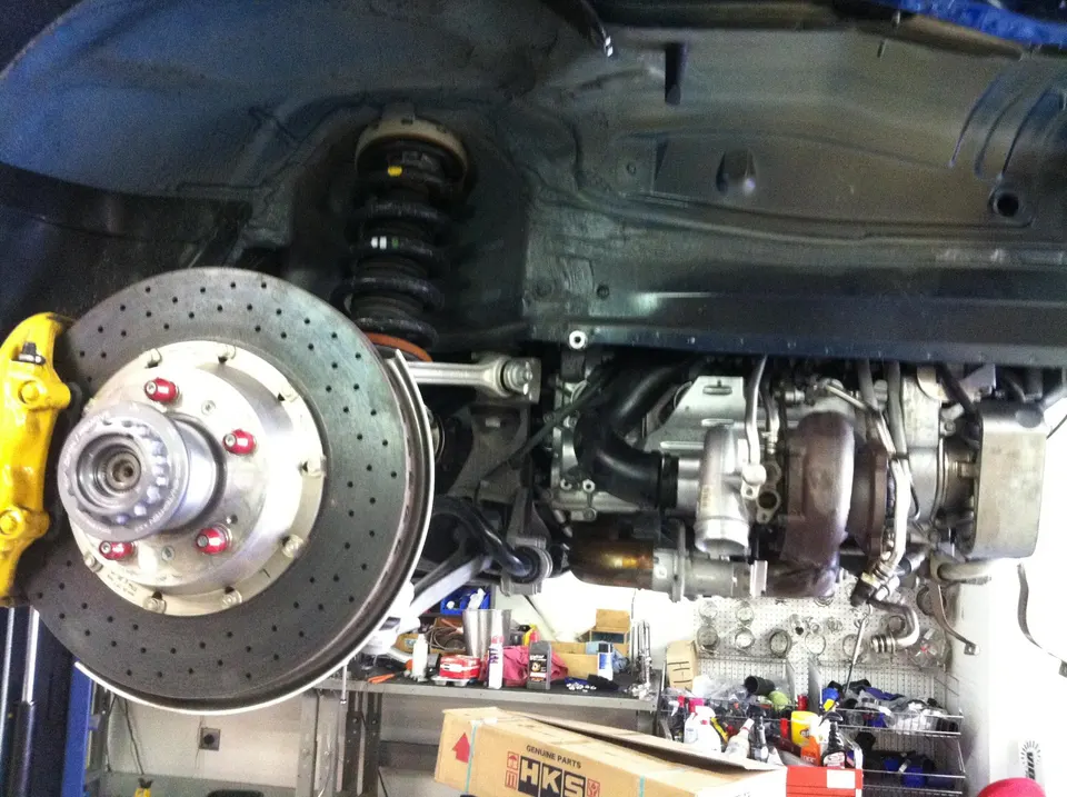 Underside view of a performance car on a lift in a shop, showcasing turbochargers, upgraded brakes, and suspension components.
