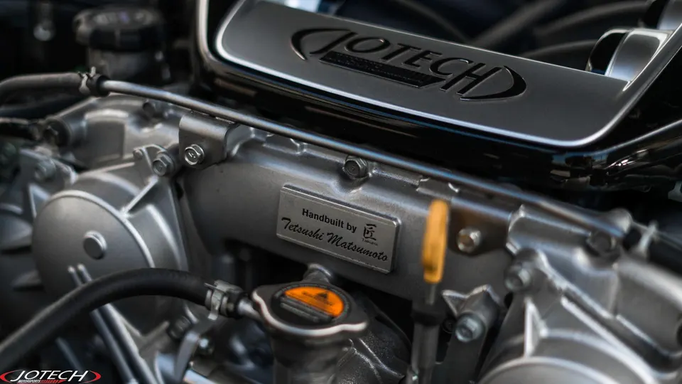 A close-up of a Jotech custom-built engine, featuring the engine cover and a "Handbuilt by Tetsushi Matsumoto" plaque.
