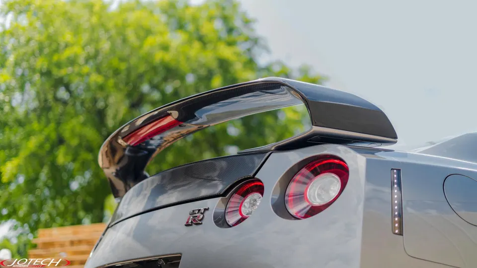 Close-up of a Nissan GT-R's carbon fiber rear wing and taillights, showcasing exterior aero modifications.