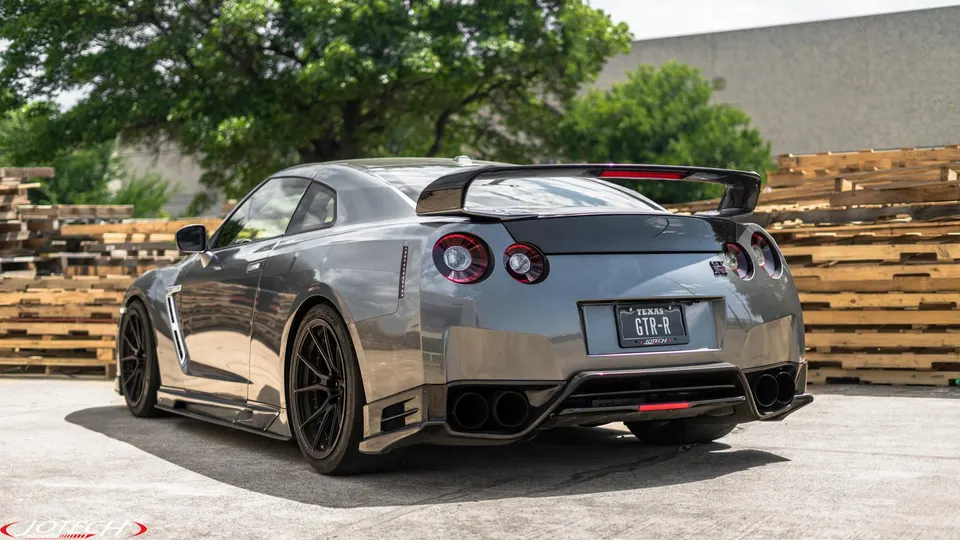 Rear view of a grey Nissan GT-R with a large carbon fiber wing and aftermarket diffuser parked outdoors.