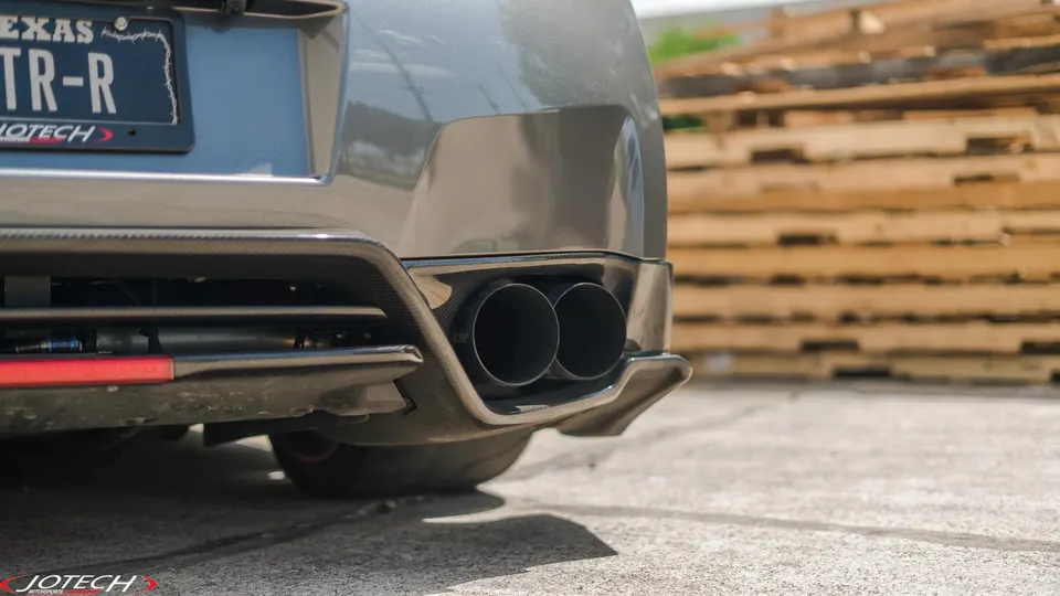 A close-up of the rear of a grey Nissan GT-R, showcasing dual exhaust tips and a carbon fiber diffuser.
