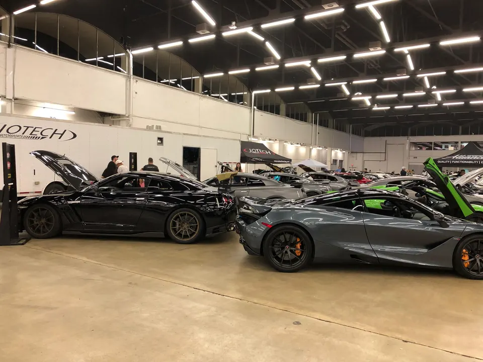Nissan GT-R and McLaren supercars on display at an indoor car show event with people around.