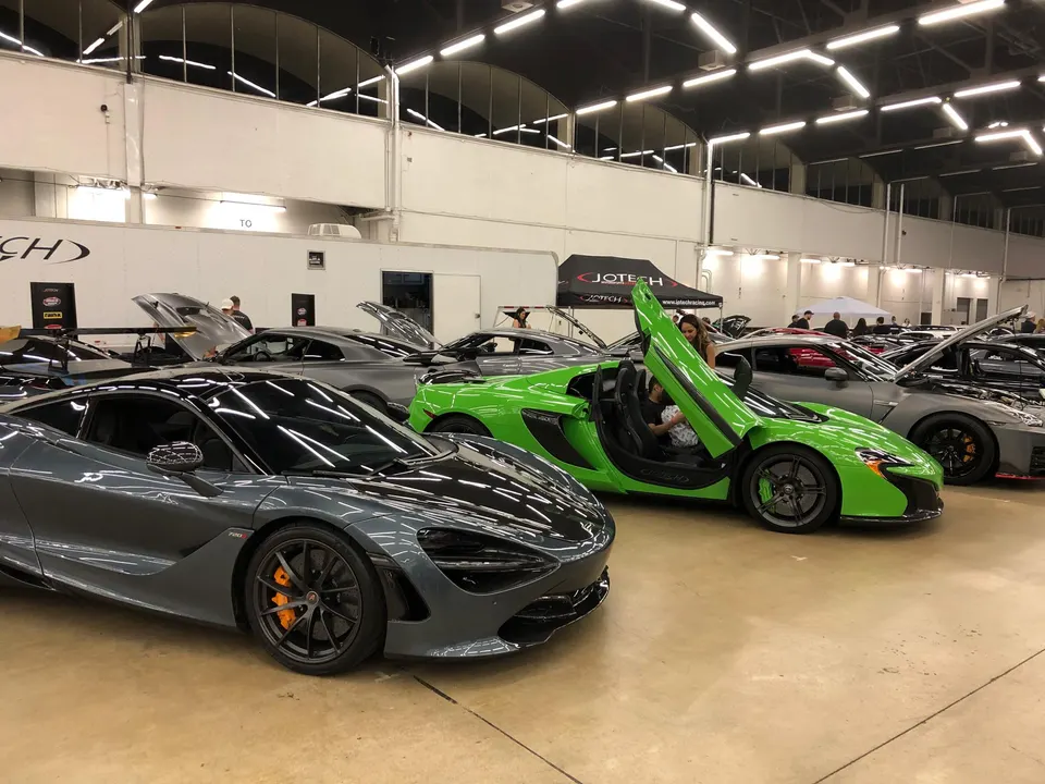 Multiple high-performance cars including a grey McLaren 720S and a green McLaren 650S on display at an indoor car show.