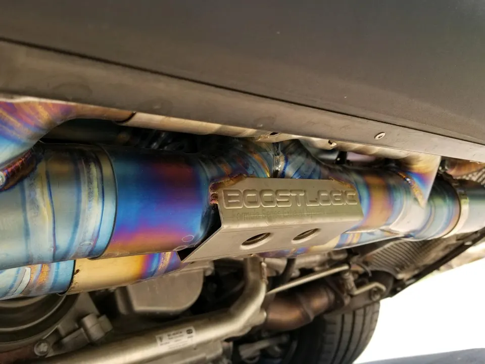 Close-up of a BoostLogic titanium exhaust system with heat-treated piping installed on a performance car.