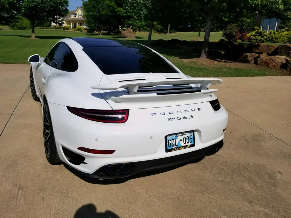 White Porsche 911 Turbo S parked on a driveway, showcasing its rear view with a prominent spoiler and quad exhaust tips.