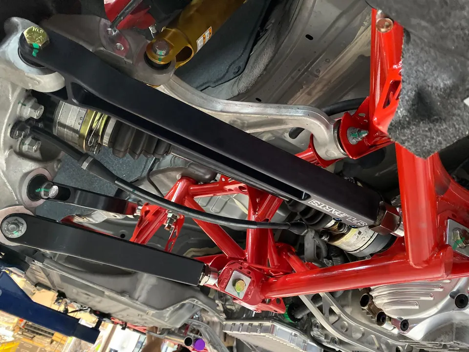 Close-up view of a car's undercarriage showing red subframe, black control arms, and drivetrain components.
