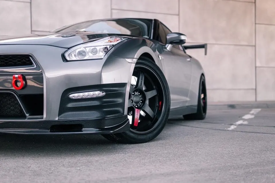 Grey Nissan GT-R with carbon fiber front lip, aftermarket wheels, and red tow hook parked outdoors.