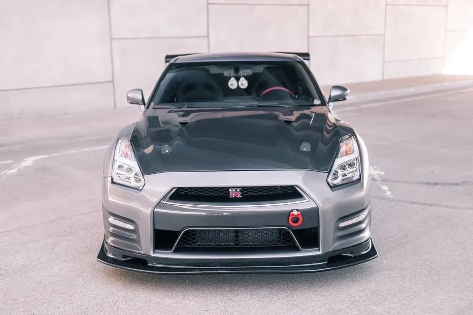 Front view of a grey Nissan GT-R with a carbon fiber hood, front splitter, and red tow hook.
