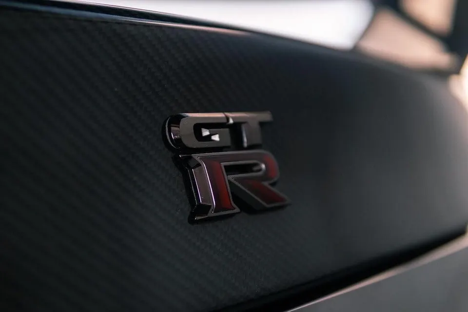 Close-up of a Nissan GT-R badge on a carbon fiber body panel, showcasing the detail and texture.