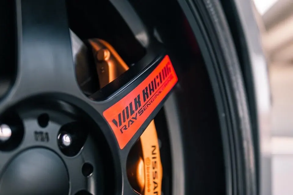 A close-up of a black Volk Racing wheel with an orange Brembo Nissan brake caliper.