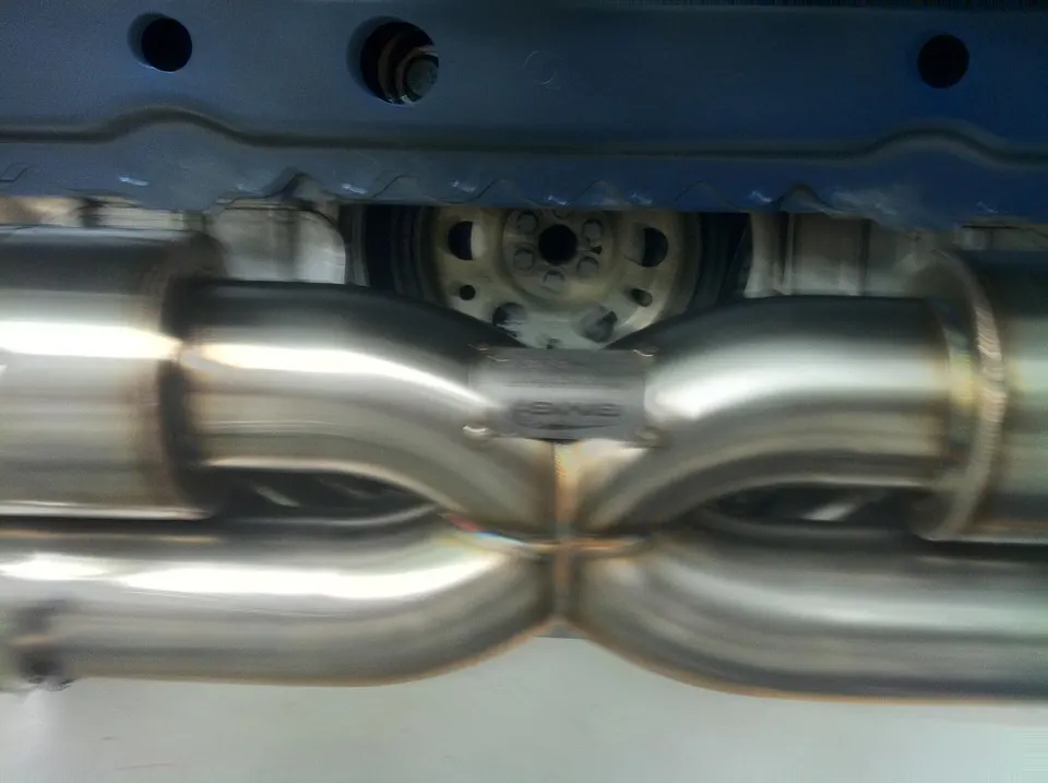 Close-up of a stainless steel performance exhaust system with an X-pipe design installed on a car's underbody.