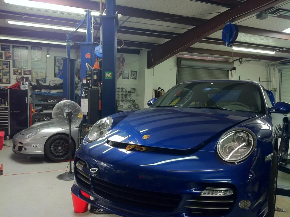 Blue Porsche 911 and silver Porsche 911 in a Jotech Motorsports performance tuning shop with car lifts.