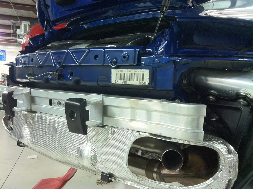 A blue car's rear bumper removed, revealing the exhaust system, heat shield, and chassis in a shop.