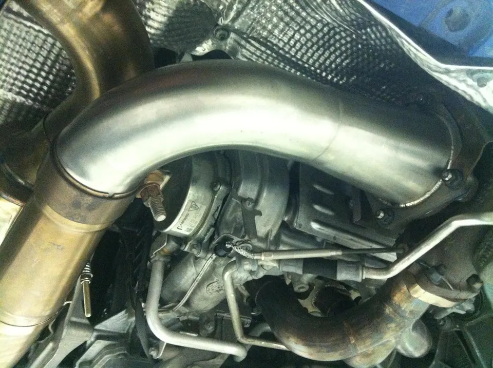 Close-up view of a performance turbocharger and downpipe installation on a sports car underbody.