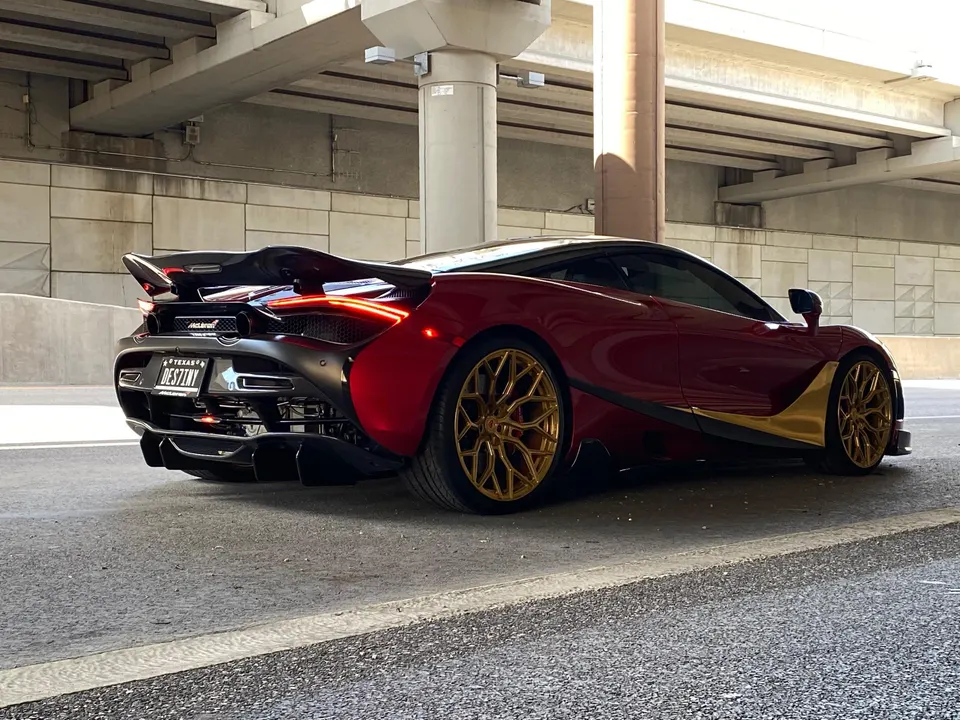 Red and gold McLaren 720S with custom gold wheels and a large rear wing parked under an overpass.