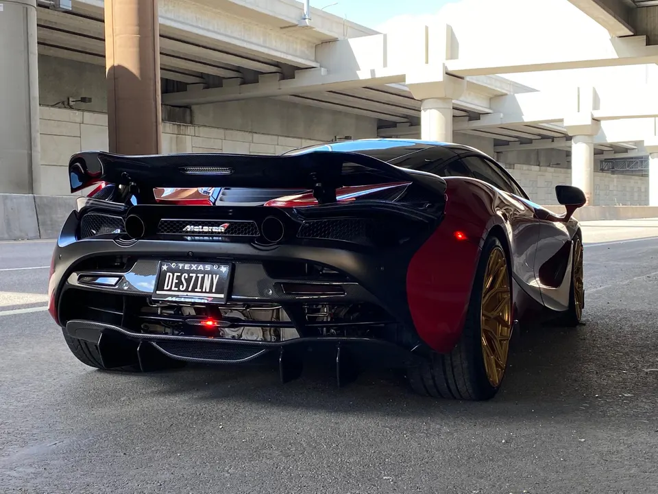 Rear view of a black and red McLaren 720S with gold wheels and a large carbon fiber rear wing parked under an overpass.