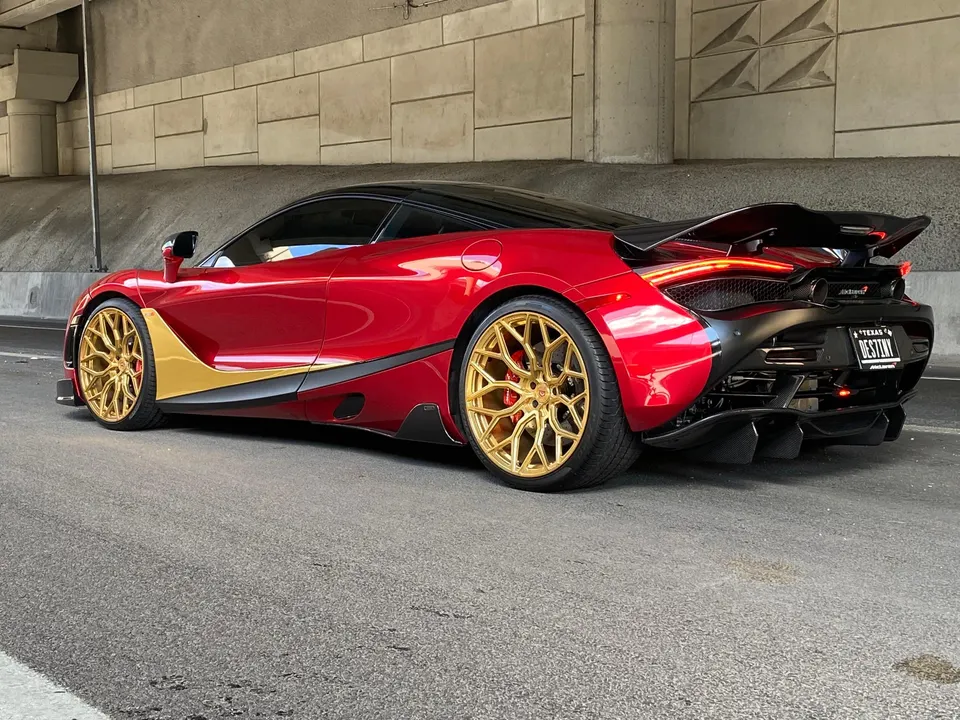 A red and gold McLaren 720S with custom gold wheels and carbon fiber aero parked under an overpass.