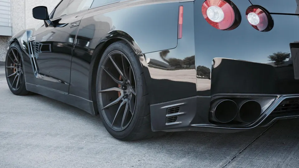 Black Nissan GT-R with aftermarket multi-spoke wheels and dual exhaust tips parked on concrete.