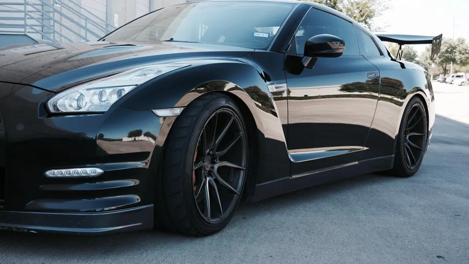 A black Nissan GT-R with aftermarket wheels and a large rear wing parked outdoors.