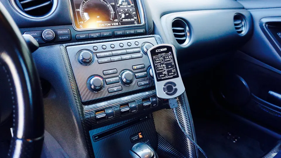 Cobb Accessport tuning device mounted in the carbon fiber interior of a Nissan GT-R, displaying engine data.
