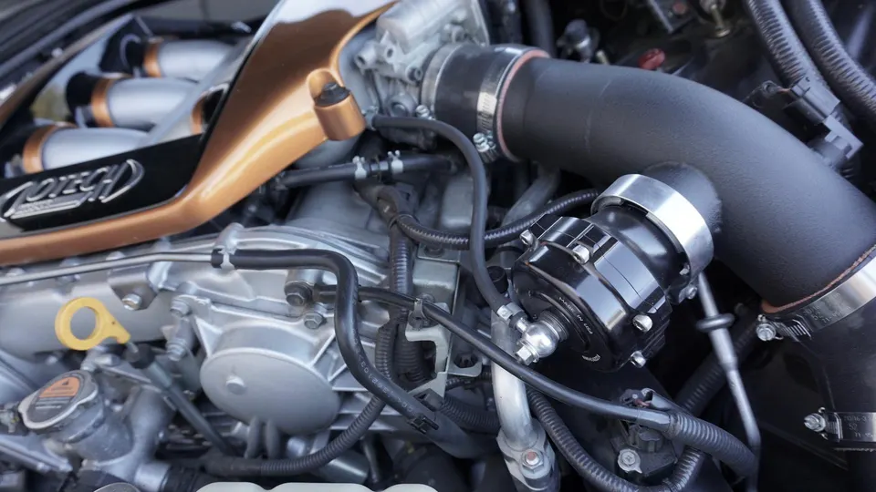 A close-up view of a Jotech custom engine bay, showcasing a gold intake manifold, black boost piping, and a blow-off valve.