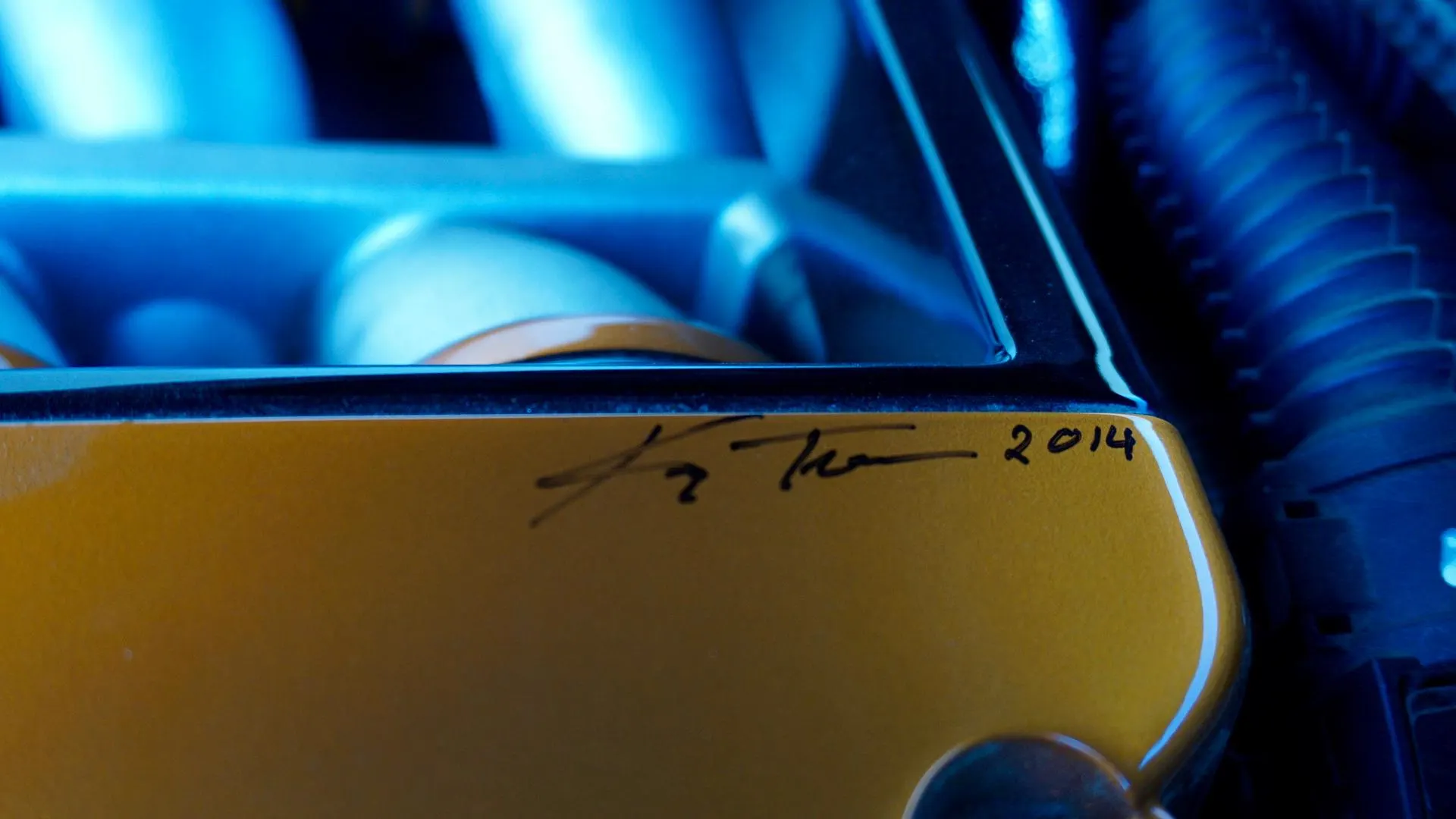 Close-up of a signed yellow custom engine part with blue lighting in an engine bay, dated 2014.