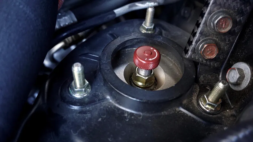 Close-up of a red suspension adjustment knob on a performance coilover in a car's engine bay.