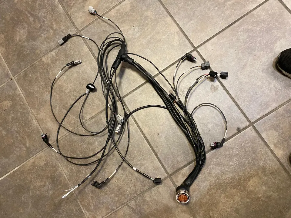 Custom wiring harness with multiple connectors and a large main plug laid out on a tiled floor, ready for a performance vehicle build.