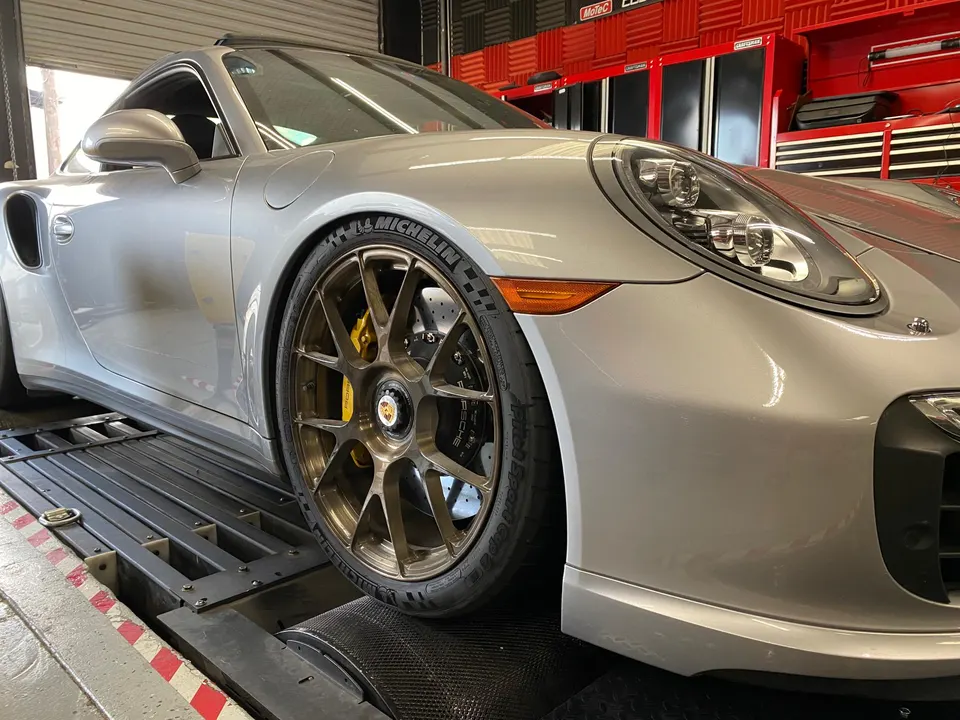Silver Porsche 911 on a dynamometer with bronze wheels and yellow carbon ceramic brakes in a performance shop.