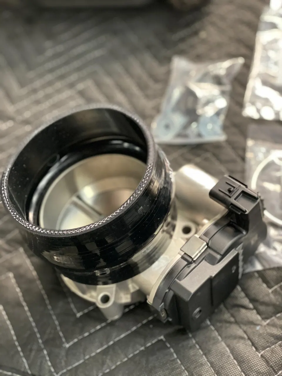 A close-up of a performance throttle body with a black silicone coupler on a quilted shop mat, ready for installation.
