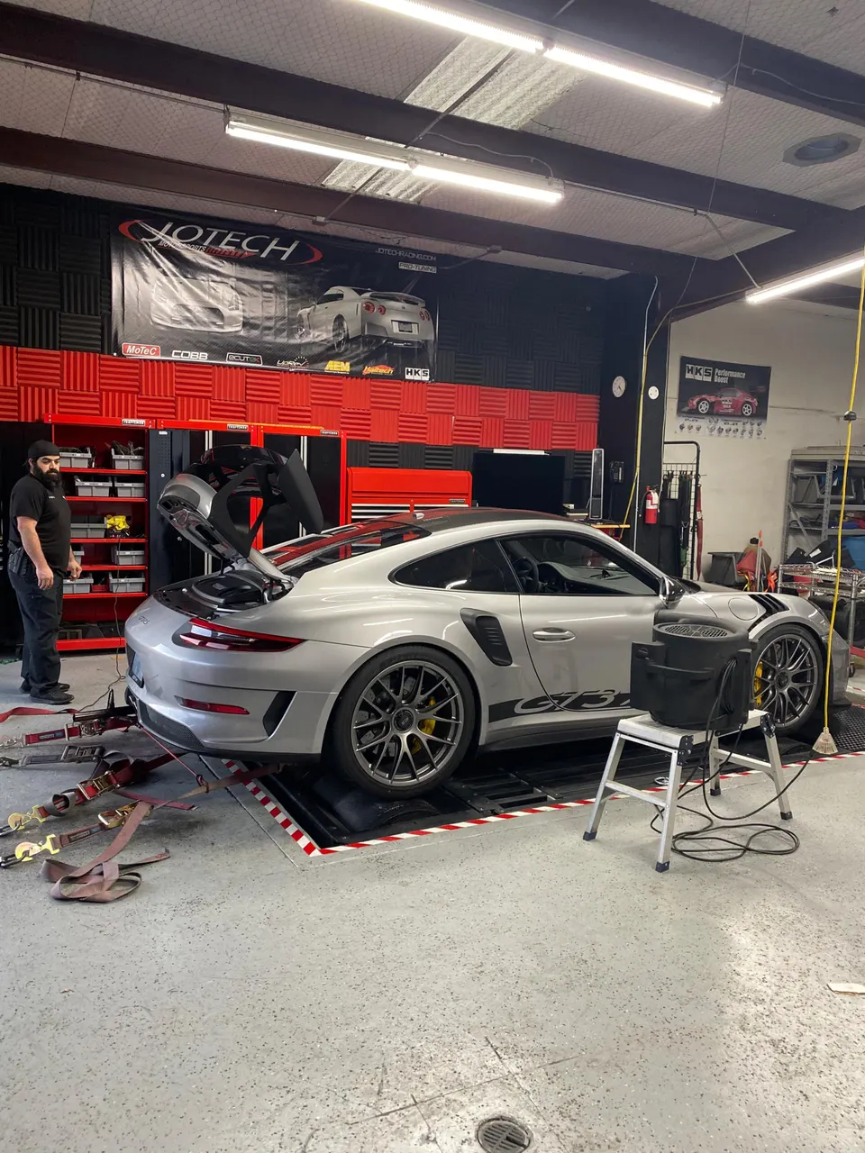 Silver Porsche GT3 RS strapped to a dyno at Jotech Motorsports for performance tuning.