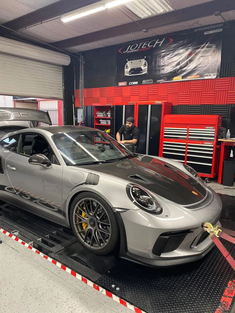 Silver Porsche GT3 RS strapped to a dynamometer at Jotech Motorsports for performance tuning.