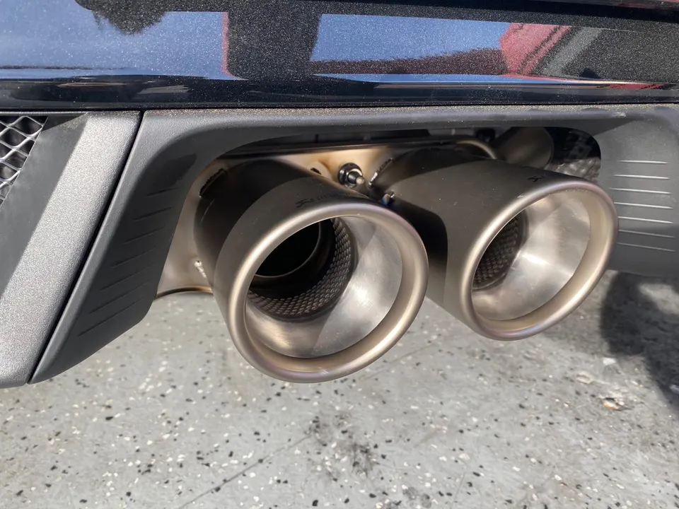 Close-up view of a car's dual performance exhaust tips, likely Akrapovic, integrated into the rear bumper.