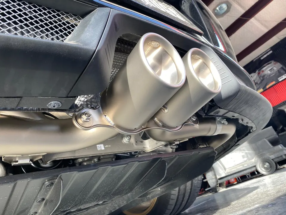 Close-up of a performance exhaust system with dual tips installed on the underside of a car in a shop.