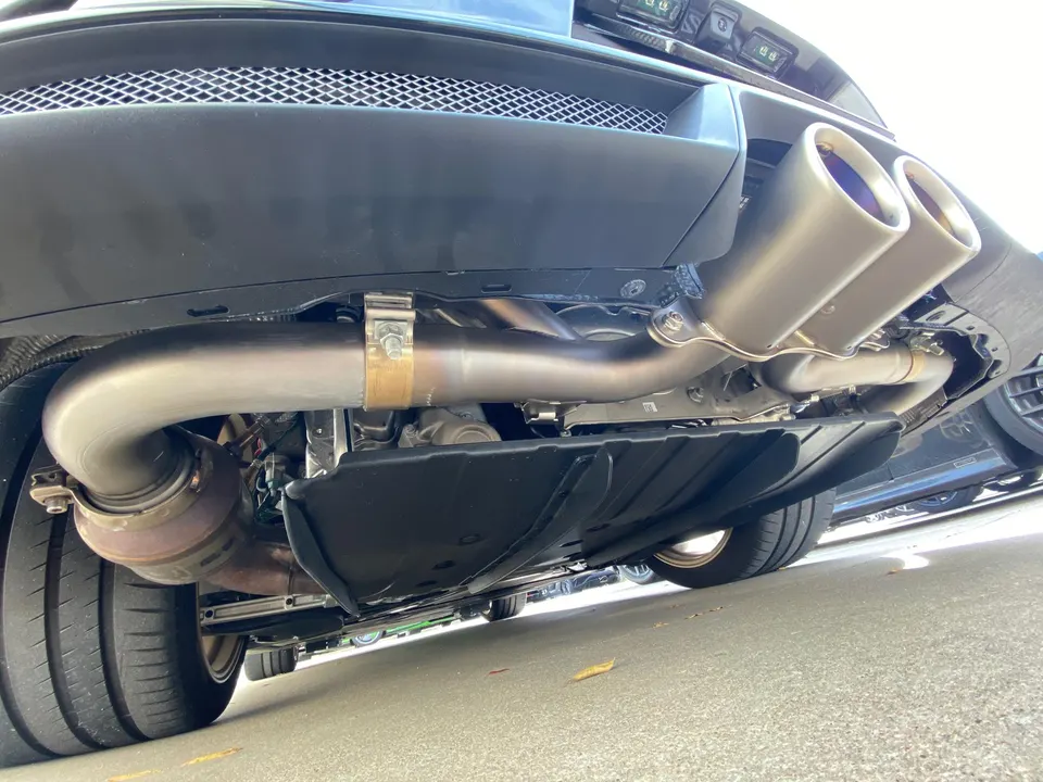 Underside view of a performance exhaust system with dual tips and catalytic converter on a sports car.